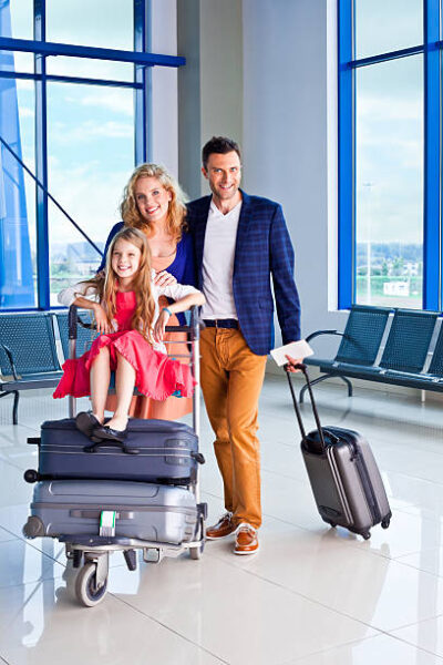 Full lenght portrait of a happy family standing with a luggage trolley and suitcases at the airport and smiling at the camera.